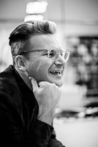 Schwarz-weiß Foto von Goran mit Brille, lachend.